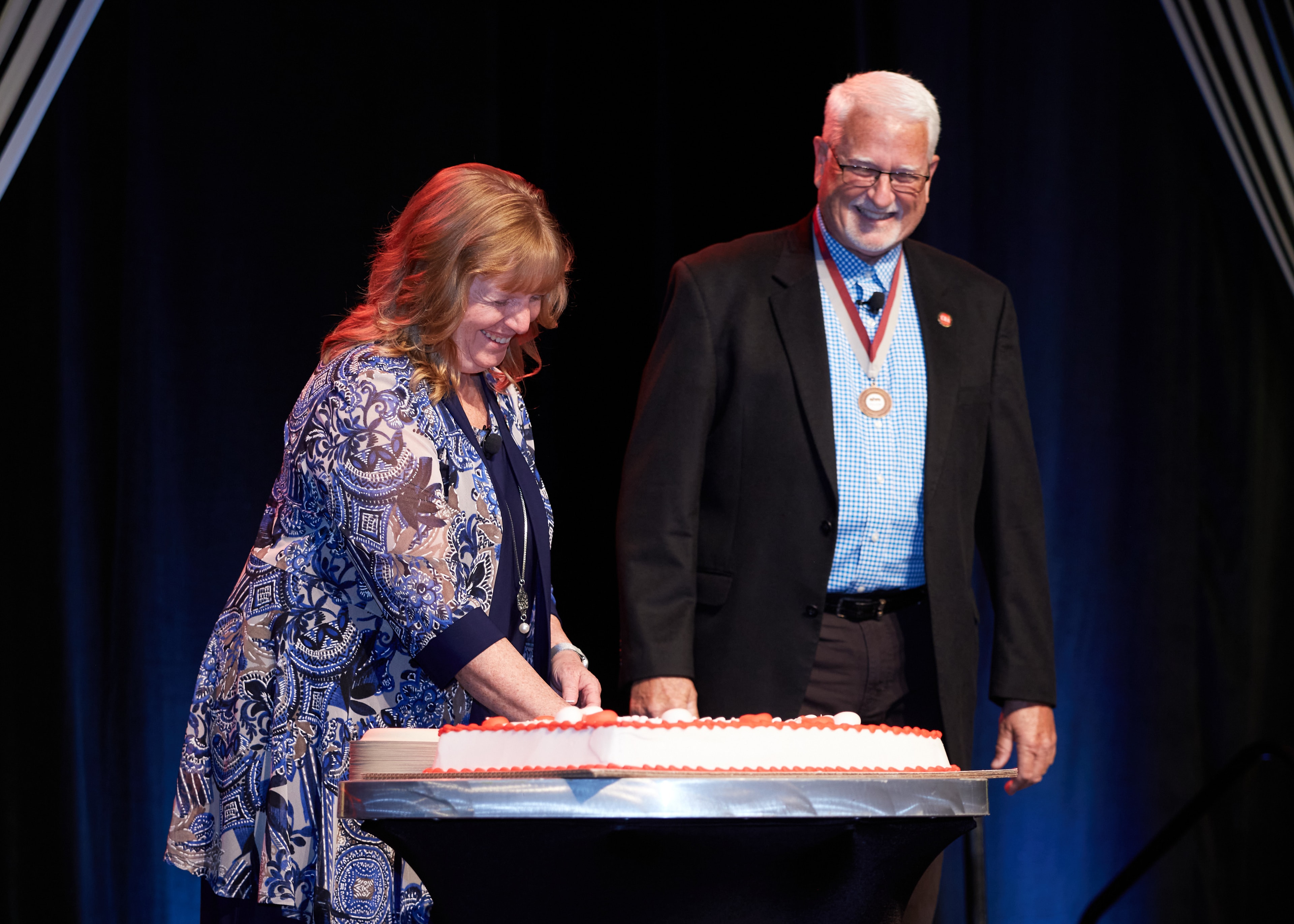 Two people cutting celebration cake on stage